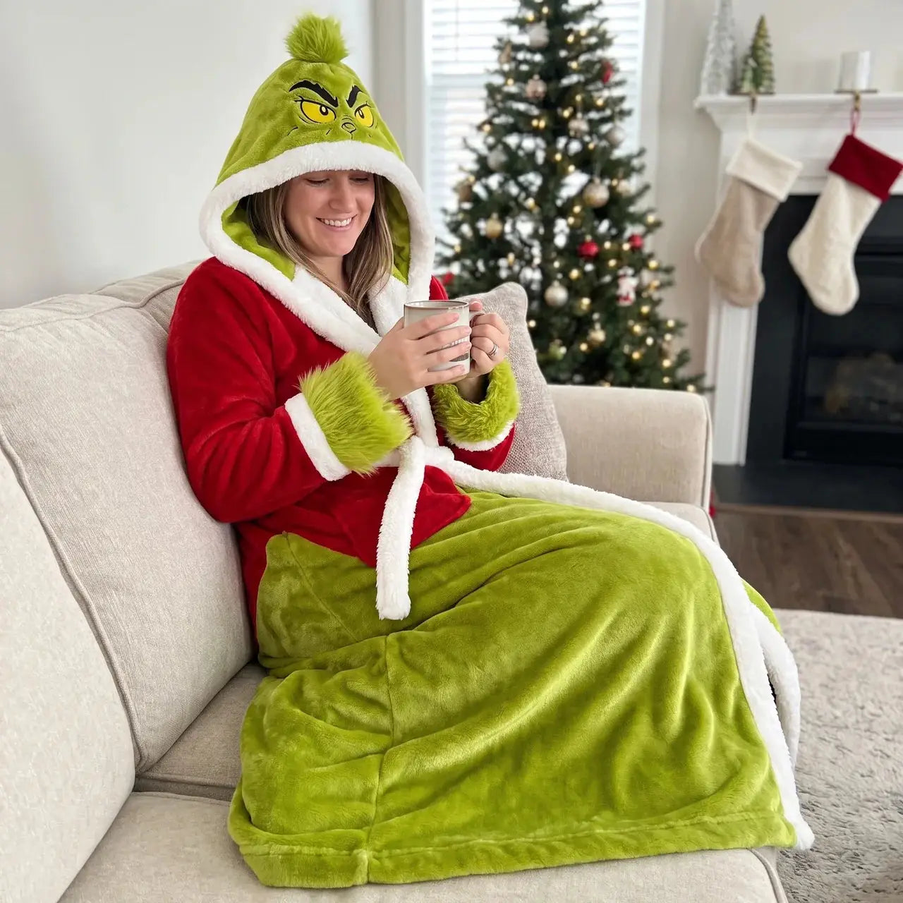 Woman in a green and red hooded heated robe holding a mug on a sofa
